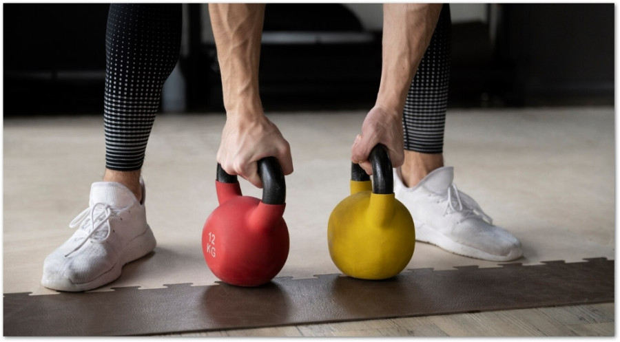 Person som lyfter en röd och en gul kettlebell på ett träningsgolv