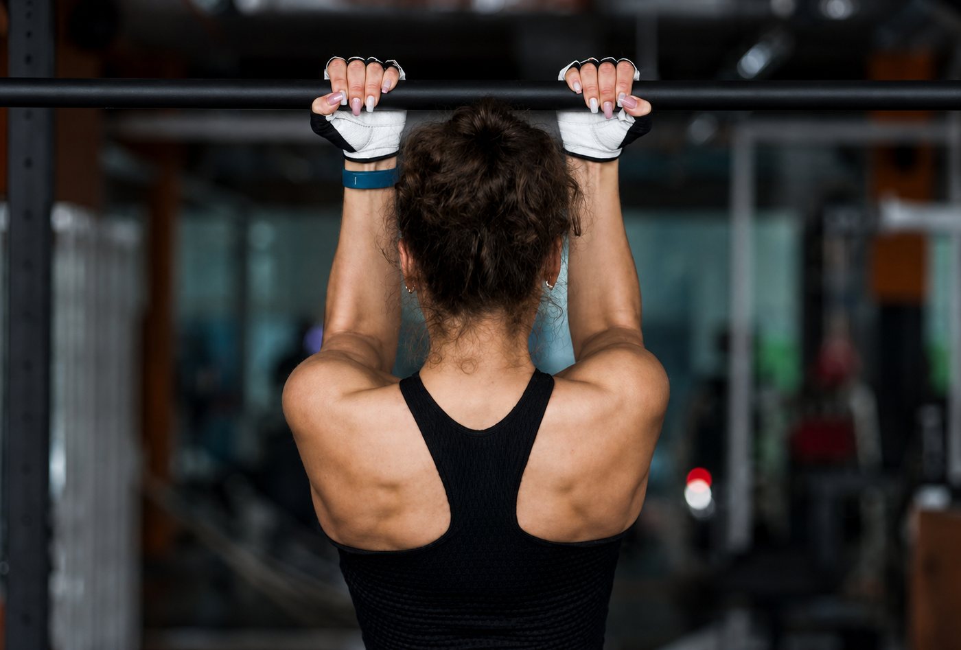 Kvinna i träningskläder och handskar som utför pull-ups i ett gym