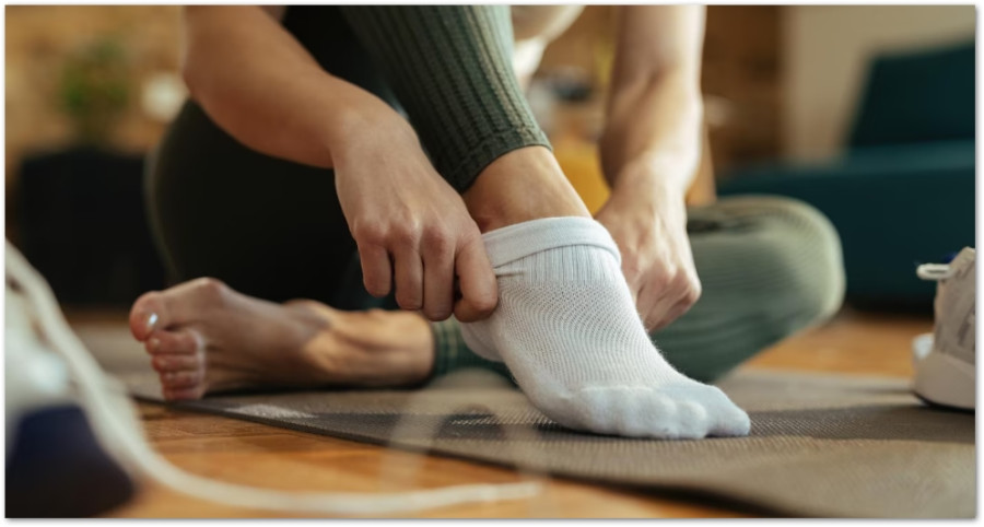 Person som drar på sig en vit träningsstrumpa sittande på en yogamatta